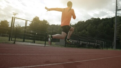 Long shot in slow motion of male athlete warming up and doing high knees juping while running on stadium. Training and exercise. 