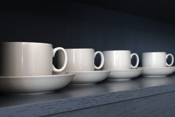 white porcelain teacups and saucers stand on a shelf with a wooden texture in blue-gray close-up