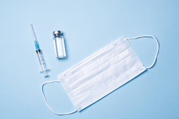 Vials with vaccine, syringe and mask on blue background, flat lay. Space for text. The concept of...