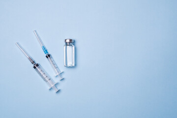 Vials with vaccine, syringe and mask on blue background, flat lay. Space for text. The concept of protection against coronavirus infection, COVID-19, vaccination. Banner