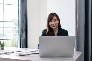 Fototapeta na wymiar Asian female finance worker working on a laptop At home office table, sit at work with happiness and smile, work from home ideas.