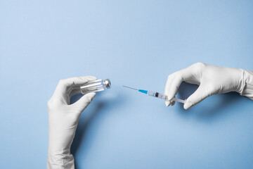 Doctor's Hand in white gloves hold the vial with vaccine or drug and syringe on blue background....