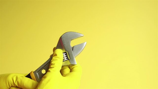 hands in yellow rubber gloves with adjustable wrench close up
