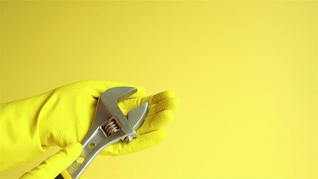 hand in yellow rubber gloves holding adjustable wrench spanner