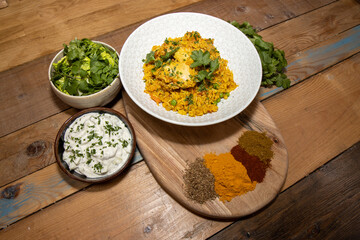 A delicious plate of Indian Curry, Chicken Biriyani surrounded with the ingredients use to make the Curry on a wooden kitchen table