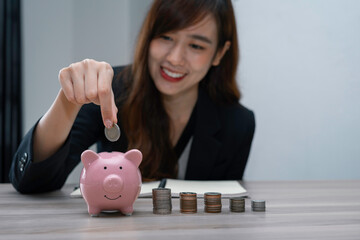 Obraz na płótnie Canvas Asian female finance businessman putting coins into a piggy bank To save money and plan for it after retirement, money saving ideas And life after retirement