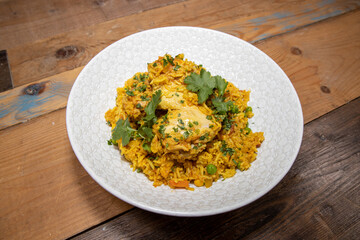 A delicious plate of Indian Curry, Chicken Biriyani topped with green coriander on a wooden kitchen table