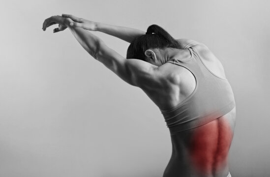 Strong sporty woman suffering from pain in back in sport wear. Sports exercising injury. Closeup portrait with highlighted in red and empty copy space. Back view. The concept of medicine, massage