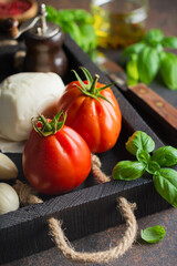 Ingredients for cooking traditional italian caprese salad ripe tomatoes, fresh garden basil and mozzarella cheese server on black board on old rustic background. Top view flat lay