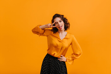 Amazing curly woman in blouse showing peace sign. Studio shot of gorgeous girl isolated on yellow background.