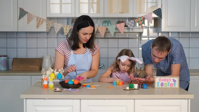 Young Mother with Little Daughter Preparing Easter Decorations while Father Holding Cute Little Rabbit in Hands in the Kitchen. Family, Easter, Spring, Happiness and People Concept