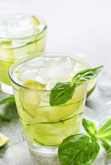 Refreshing summer homemade lemonade made from lime, lemon, cucumber and basil with ice in glass on old concrete background. Selective focus.