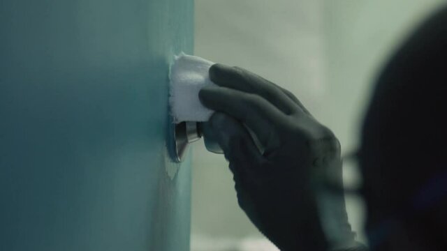 Manos con guantes sanitizando la perilla de una puerta