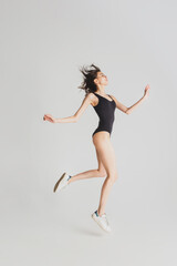 Fototapeta na wymiar Jumping. Beautiful young woman's isolated on white studio background. Having fun, happy, full length. Dancing, getting crazy mood, stylish posing. Fit girl in black sportive swimsuit. Copyspace.