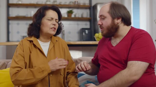 Young man helping senior mother with heart attack sitting on couch