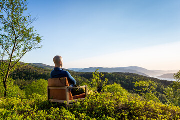 A man sitting and relaxing in a chair, looking out over the forest and landskape