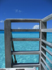Fototapeta na wymiar Wooden ladder down to the sea. Clear water looks like a pool. Blue sky, white clouds,