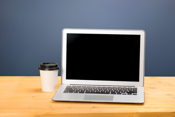Fototapeta premium Mockup blank laptop screen with coffee on wooden table in coworking space.
