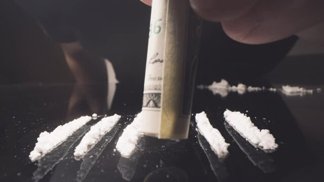 Cocaine junkie snorting line of coke with rolled US dollar bill. Drug Addiction.