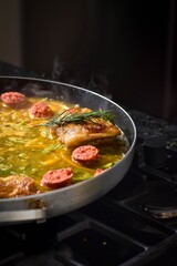 preparing a stew with chicken, chorizo, onion and rosemary on a black frying pan