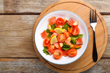 Salad with salmon and cherry tomatoes and green salad in a plate on a wooden table on a wooden stand stand next to a fork.