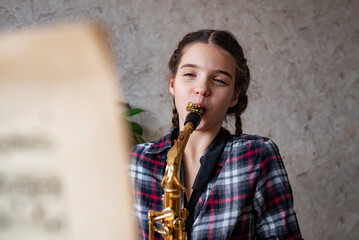 The girl learns to play the saxophone. The child is studying music at home.