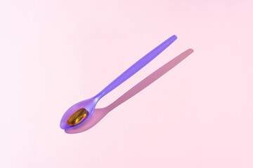 Fish oil tablet on purple plastic spoon.