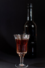 an alcoholic drink in a glass with edges and a bottle on a black background