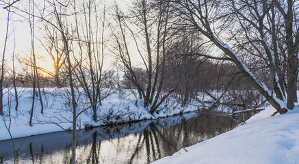 Snow-covered banks of a small river at sunset