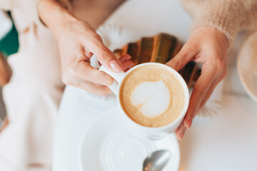 Girl in a cafe with a hot cup of latte coffee and croissant