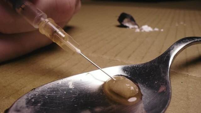 Closeup Syringe needle extracting heroin from a spoon after cooking using filter