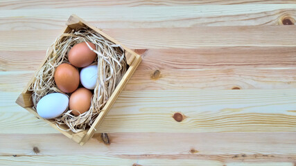 Straw and eggs in wooden crates on wooden background with copy space.