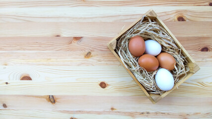 Straw and eggs in wooden crates on wooden background with copy space.