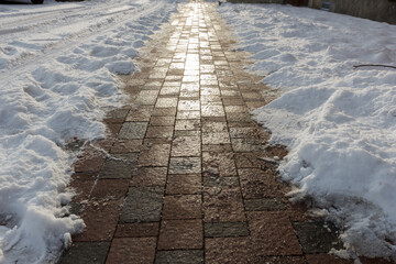 A sidewalk after snowstorm is cleared of snow. In evening sun light.