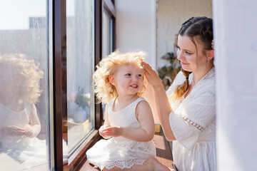 Mother and daughter on the windowsill looking out the window. Happy family at home on the background of a large window.