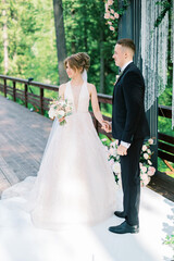 Fashionable newlyweds stand at wedding arch. Bride in Wedding dress and groom in black tuxedo....