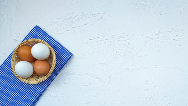 Straw and eggs in wooden crate in blue checkered cloth on white stucco concrete floor with copy space.