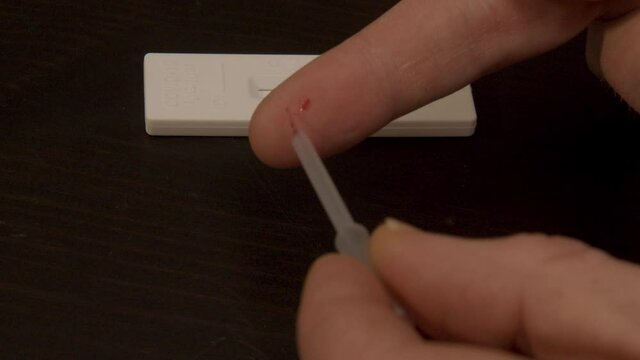 pipette sucking up drop of blood from finger in preparation of Covid-19 self test - close