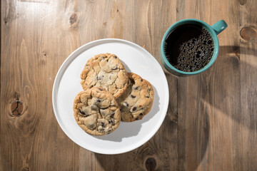 Chocolate chips cookies on a plate with coffee in a mug.