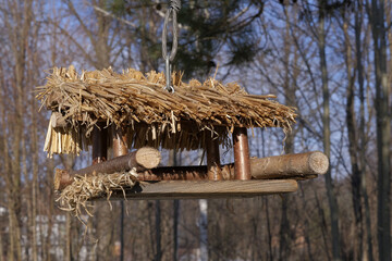 A bird feeder - in the form of a hut hanging from a pine branch, on a sunny winter day.