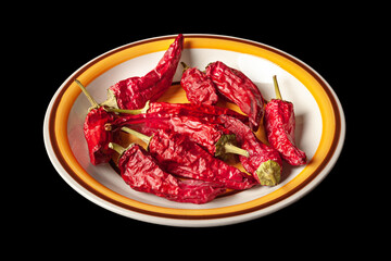 Red dried chili peppers in a round plate. Heap of hot dry peppers on a black background.