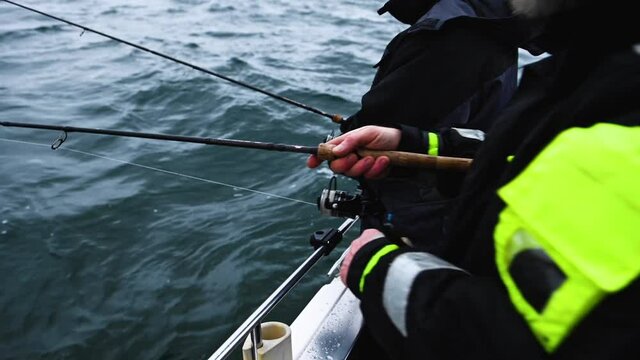 Two anglers jigging cod on a small boat out on the open sea. It is a grey, overcast winter day. The waves make the boat rock up and down. 1080p