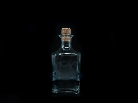 Single empty glass bottle on a black background. Transparent square bottle. Front view of the laying on its side transparent square bottle.