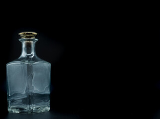 Empty glass bottle closed with big golden round cork isolated on a black background. Transparent square bottle. Front view of the vertical staying jar.