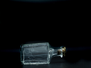 Single empty glass bottle on a black background. Transparent square bottle. Front view of the laying on its side transparent square bottle.