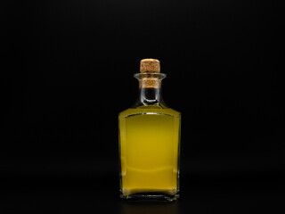 Glass bottle with alcohol drink closed with cork cap isolated on a black background. Transparent square bottle with yellow liquid. Front view of the vertical staying jar.