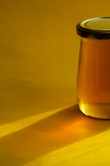 Natural sugar substitute, healthy food concept. Raw bee honey in glass jar on yellow background.