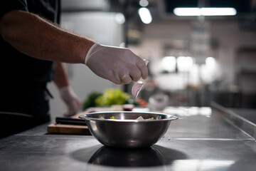 chef cook hands in gloves prepare salad and adding red onion in bowl at kitchen