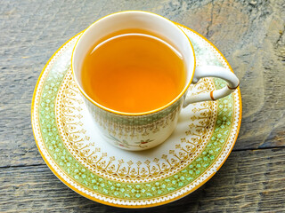 Hot tea in vintage picture of antique hot tea cup in saucer on wood background