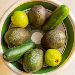 Top view of fruit bowl with four avocados, two cucumbers and two guavas on a beige background, combination of fruits and vegetables with green peel. Concept of bio, biological and natural cultivation